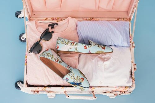 Offener Koffer mit Kleidung auf Holzboden nach der Urlaubsrückkehr